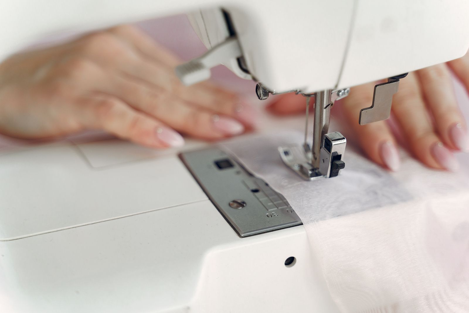 A seamstress working at a white home sewing machine in a well-lit workspace