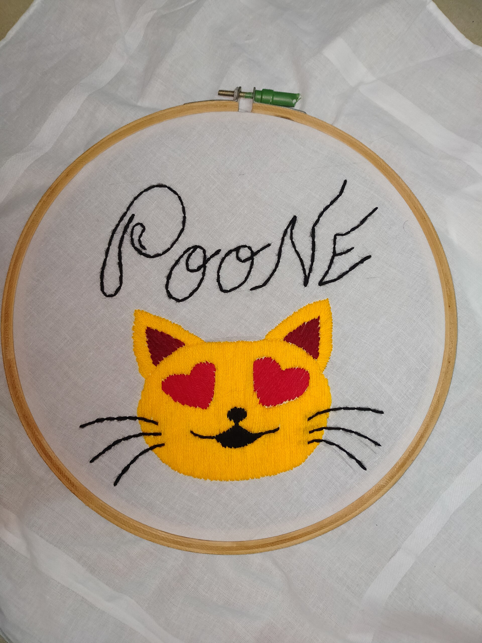 A small embroidered cat design in a round embroidery hoop with green border fabric