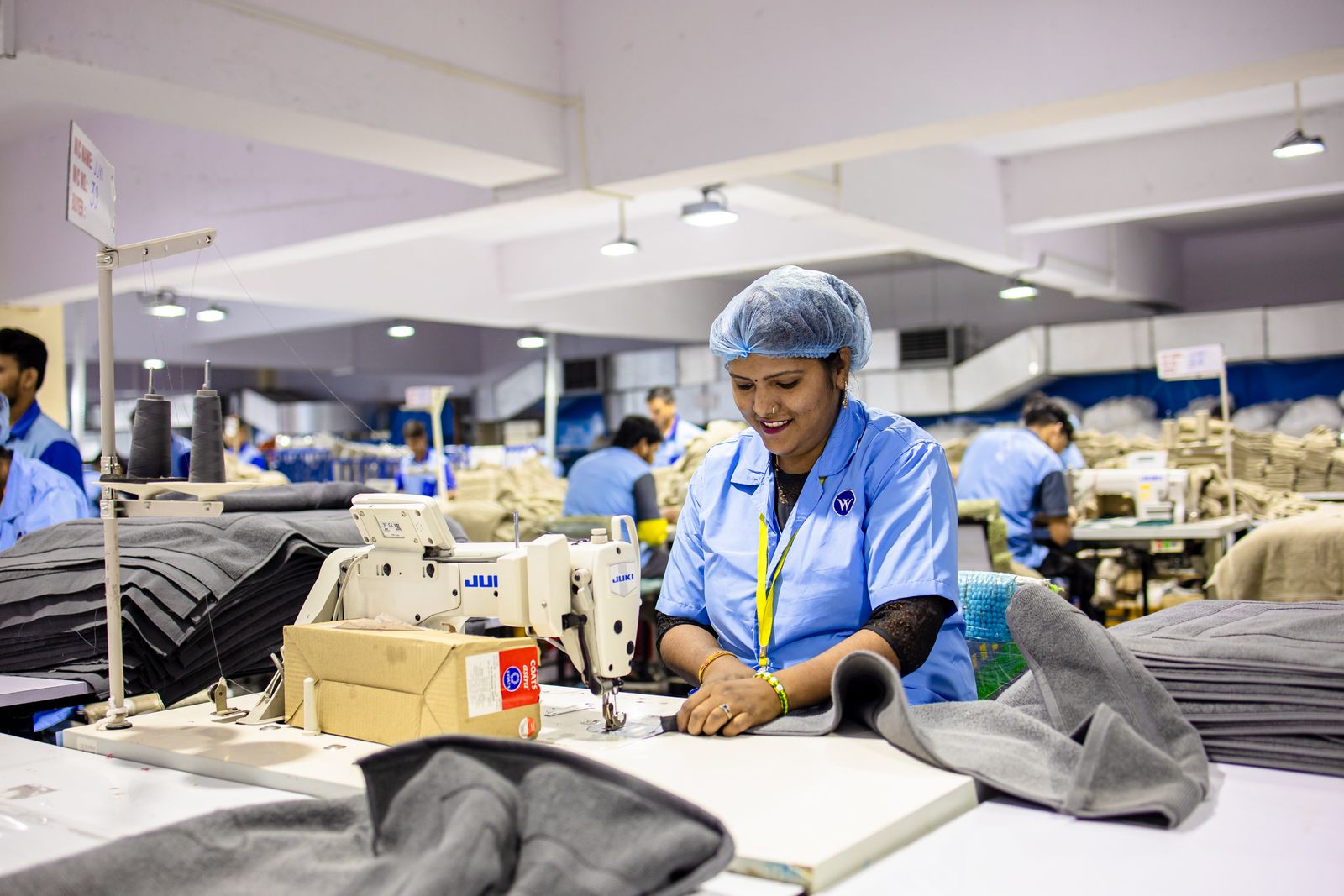 Workers operating multiple industrial sewing machines side by side in a production facility