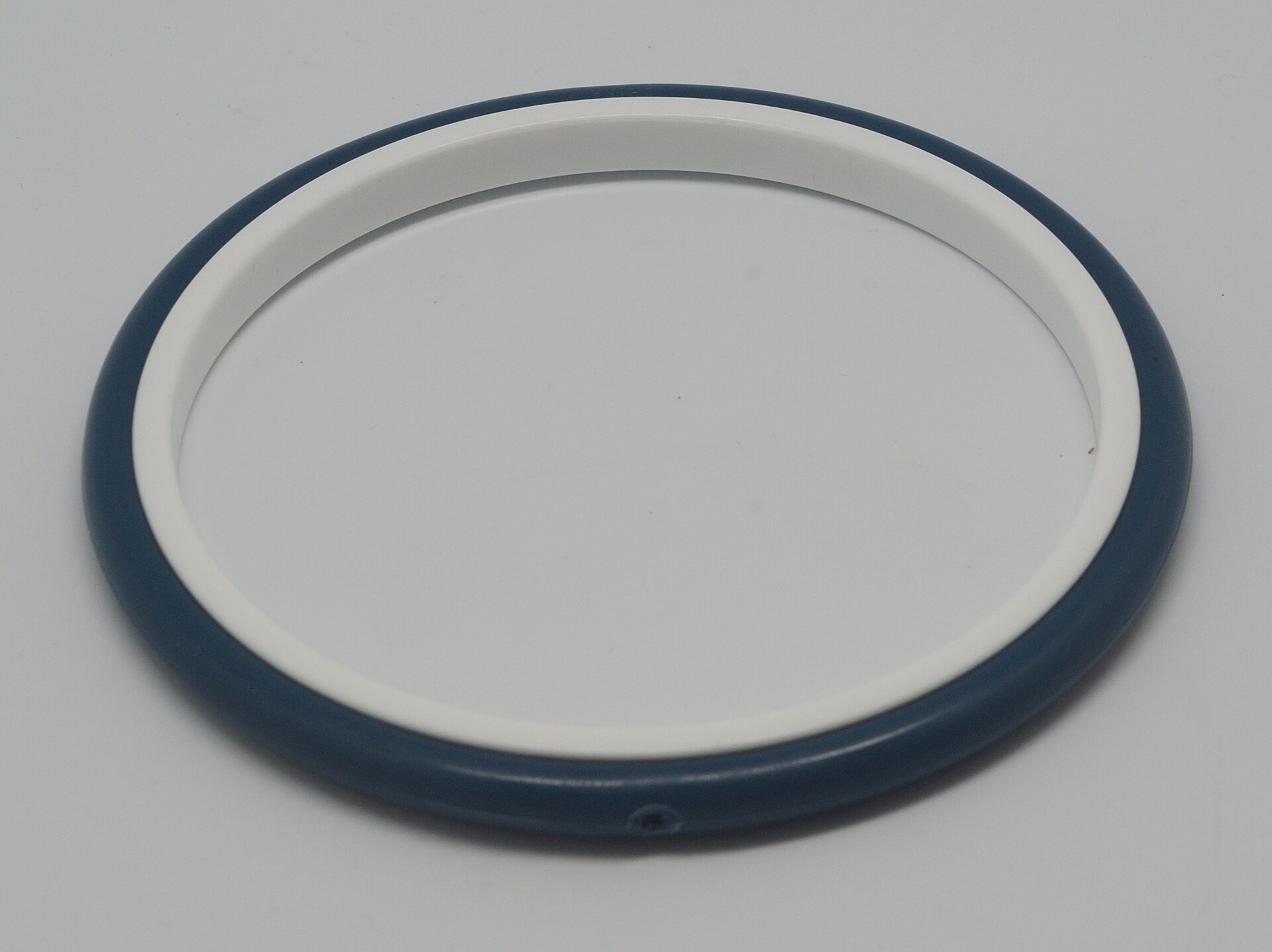 A plastic embroidery hoop with green fabric stretched between the inner and outer rings