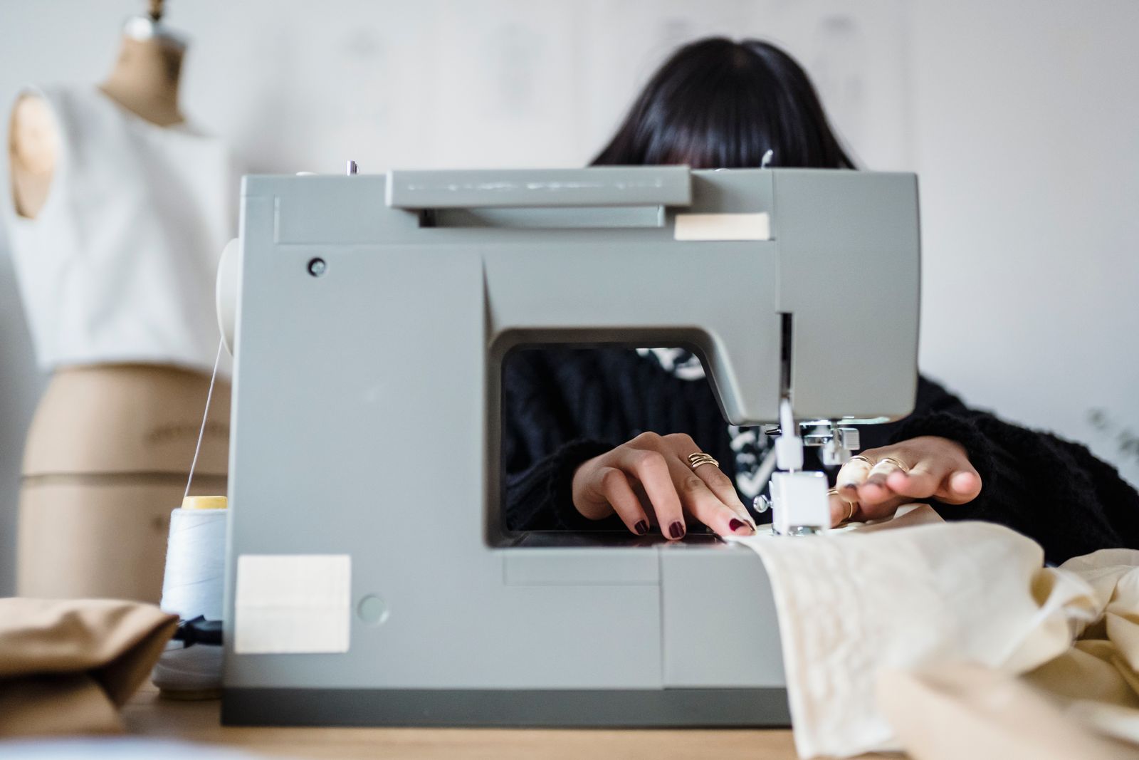 A woman at a sewing machine in a workshop setting guiding fabric under the needle