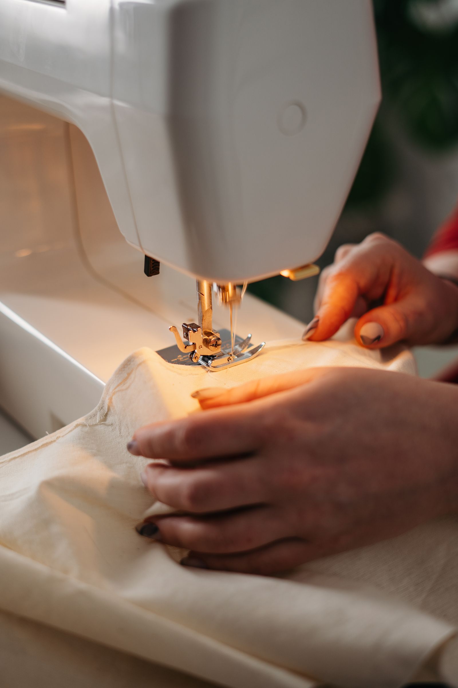 Hands guiding fabric under a sewing machine presser foot, with stabilizer backing beneath the fabric