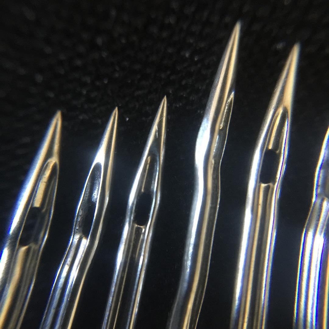 Close-up macro photograph of sewing machine needles showing the needle shaft, eye, and flat side in detail