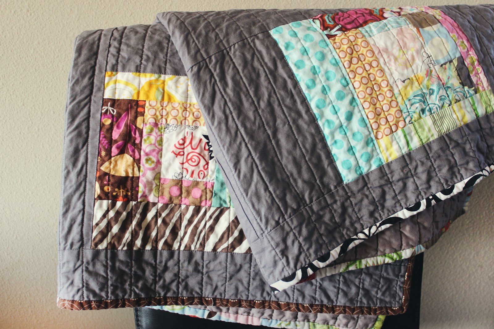 Handmade patchwork quilt in gray, blue, pink, brown, and yellow geometric blocks draped over a chair