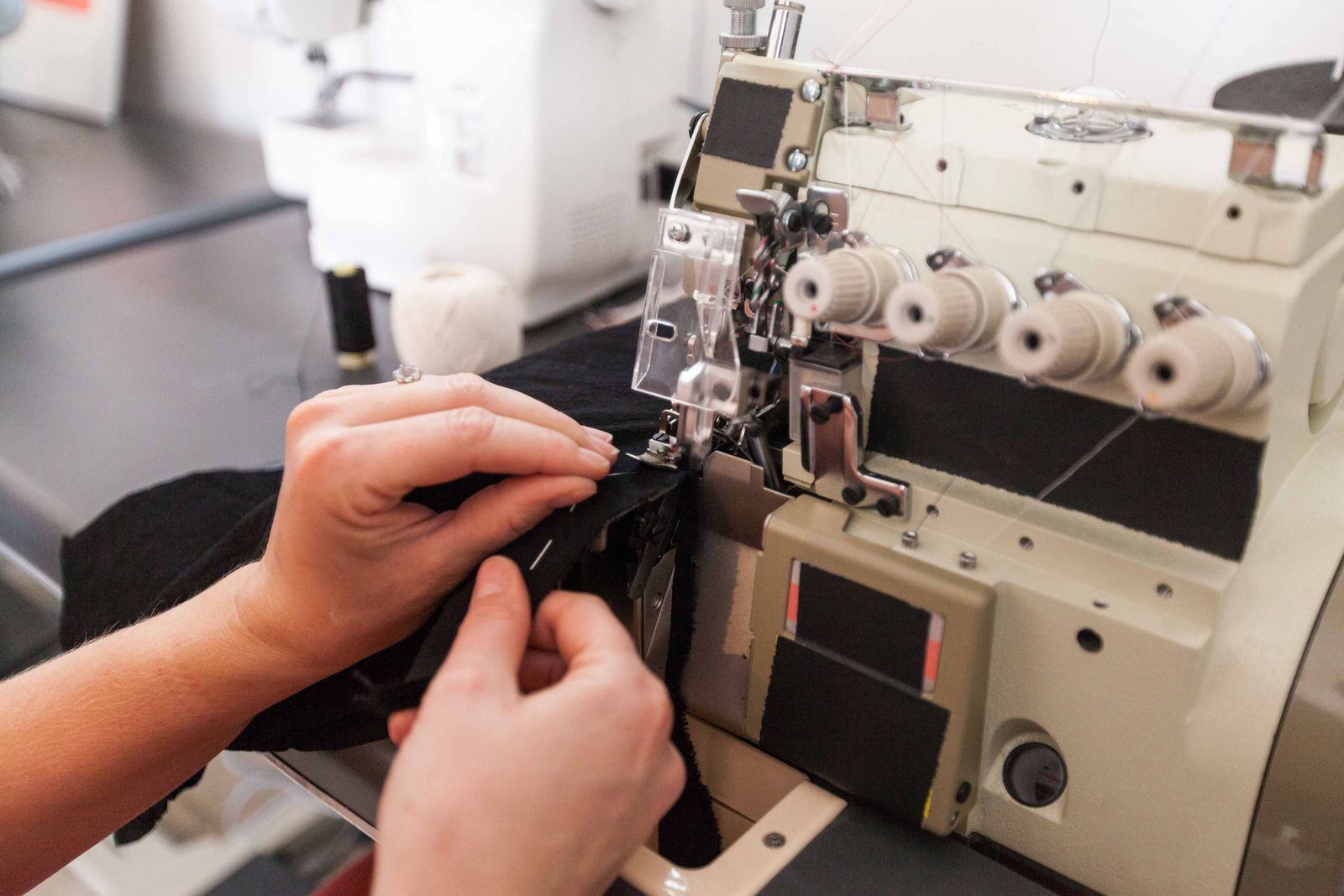 Hands operating an overlock serger machine, guiding fabric through the needle plate and looper
