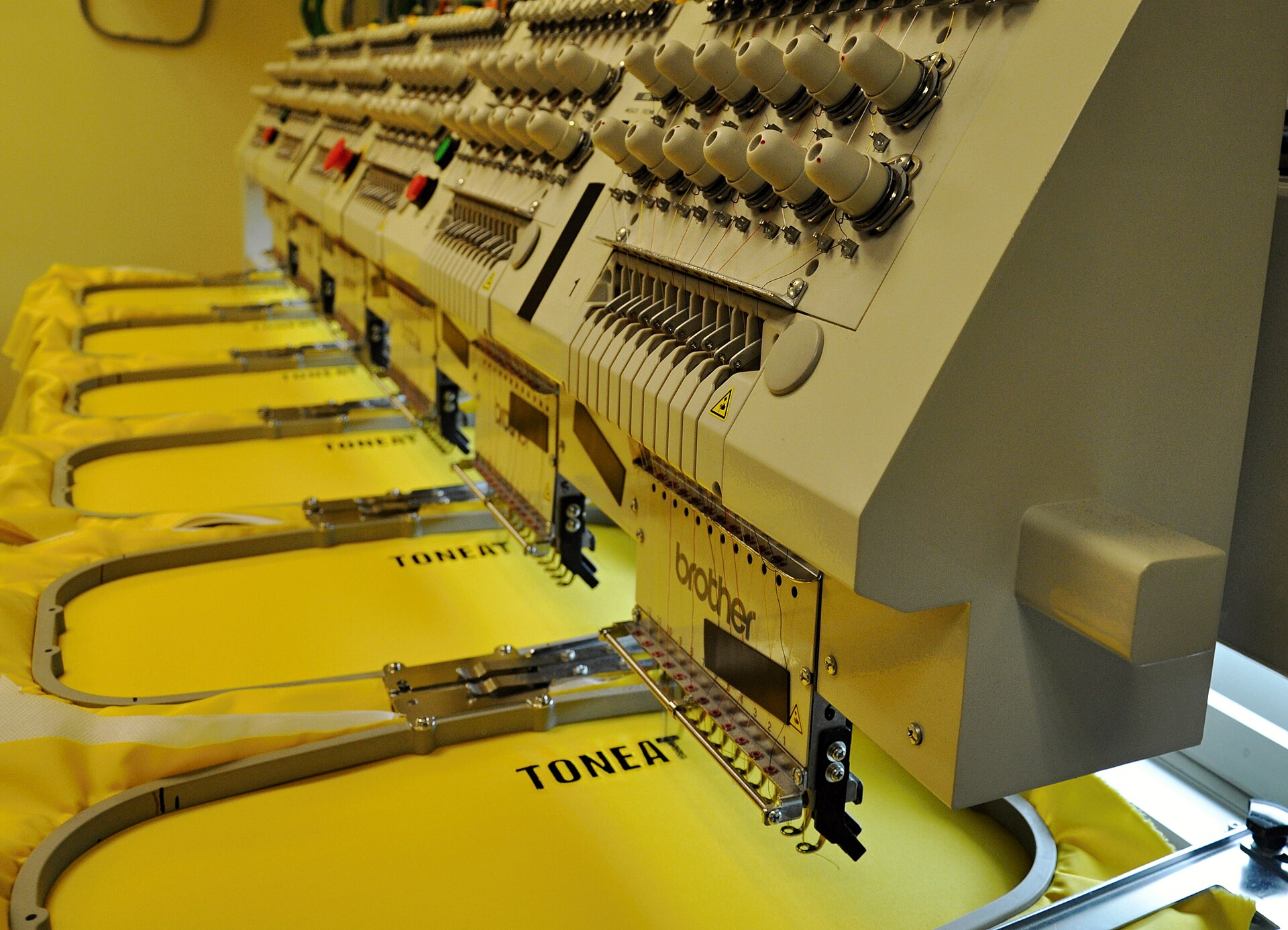 A modern multi-needle commercial embroidery machine in operation showing multiple thread paths and needle bars