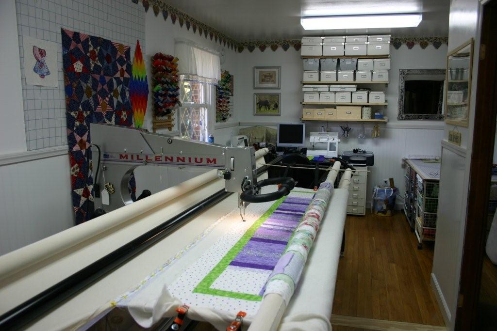 A longarm quilting machine head mounted on its metal rail frame with a quilt in progress stretched across the frame